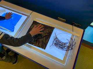 view from behind of child touching bags with blue water, mud, and sticks in bags on light panels