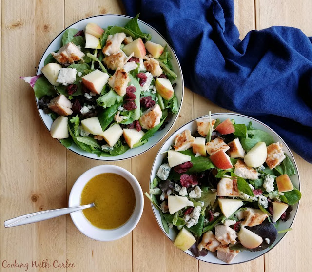 The crunch of fresh apples, the sweetness of dried cranberries, savory chicken and cheese, and fresh greens come together in this great salad that helps bridge the seasons when you still want something light but fall flavors are calling your name! The homemade dressing is perfect for all kinds of salads as well! bowls of salad with chicken, cranberries, cheese, apples and homemade salad dressing