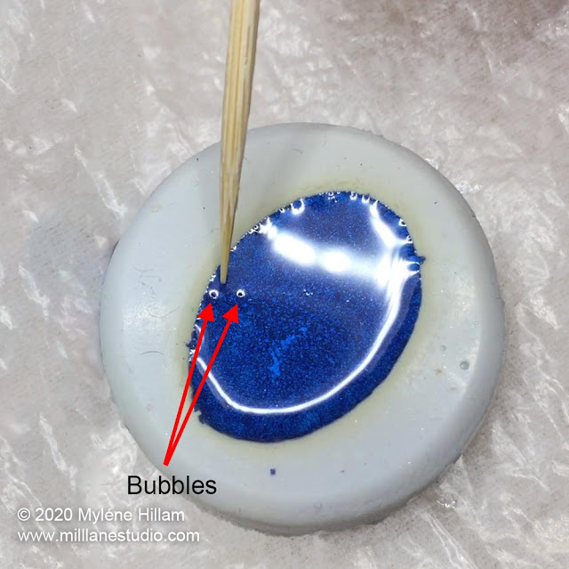Using a toothpick to drag bubbles to the edge of the mould.