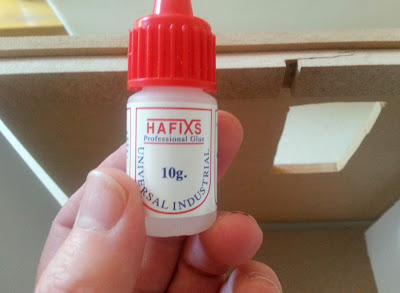 Bottle of Hafixs professional glue held up in front of a mended beam in a dolls' house kit.