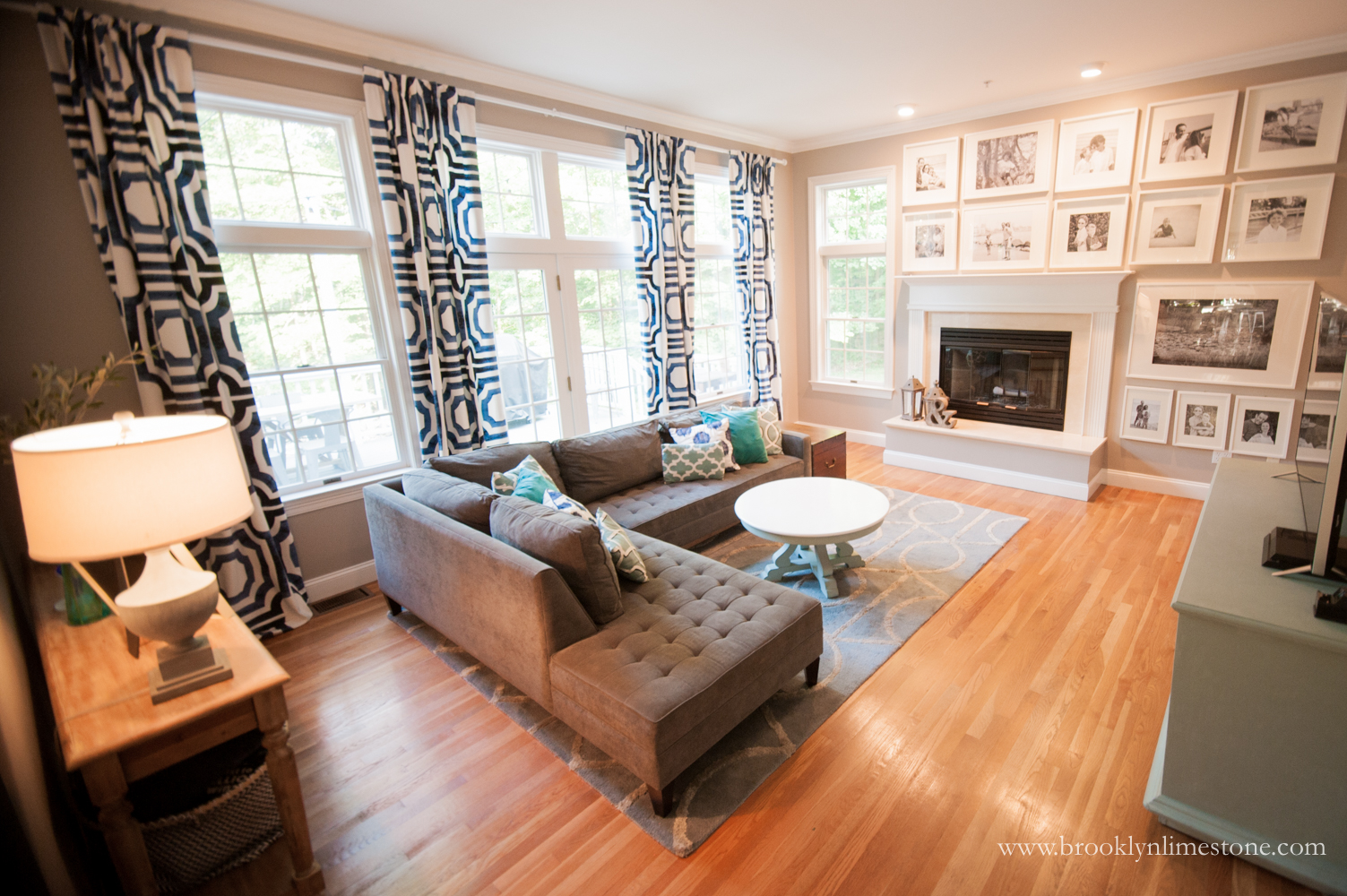 Family Room Makeover after - Blue and White Curtains added to Window Wall, Sectional Sofa against the left wall, console and TV on the right wall and white Ikea frames on the entire wall surrounding fireplace to balance it out