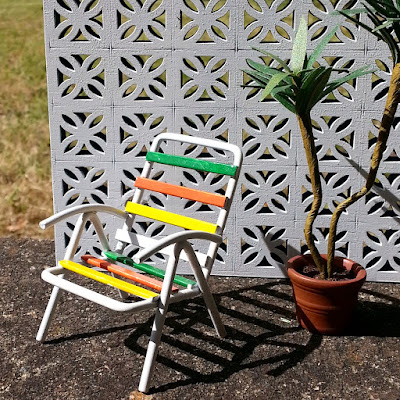 One-tweltfh scale modern miniature garden chair and plant in front of a miniature breeze block wall.