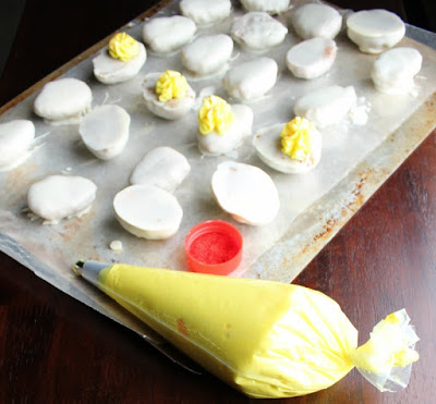 egg half cake balls dipped in almond bark with piping bag of yellow frosting and red sugar