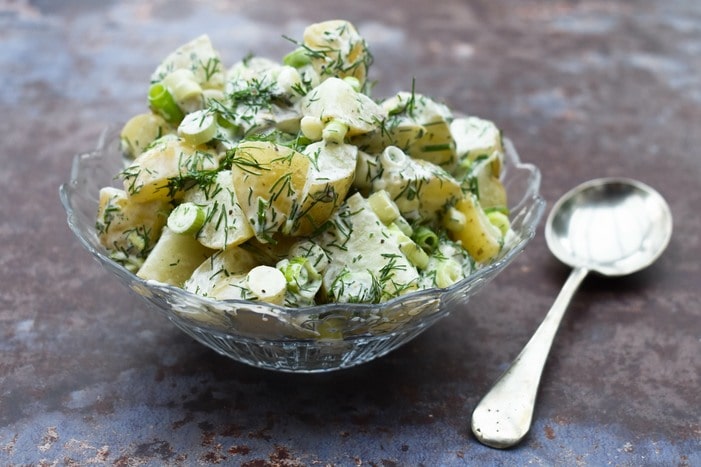 creamy potato salad in a glass bowl on a granite surface