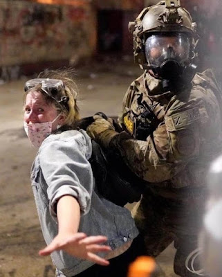 Man in battle gear dragging away woman in mask