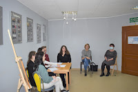 Grupa młodzieży siedząca w czytelni Biblioteki w Zelowie na tle wystawy o Vaclavie Havlu.