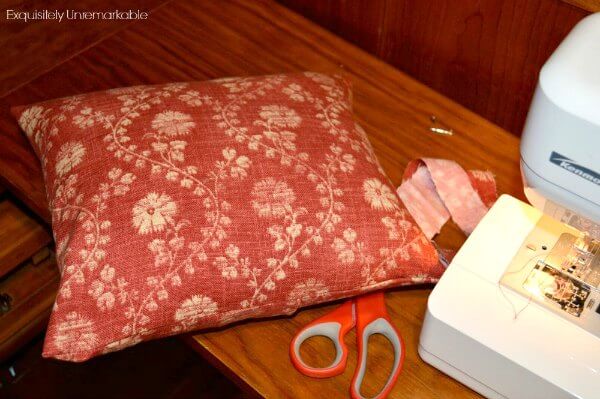 Red pillow on table with sewing machine scissors and scrap fabric