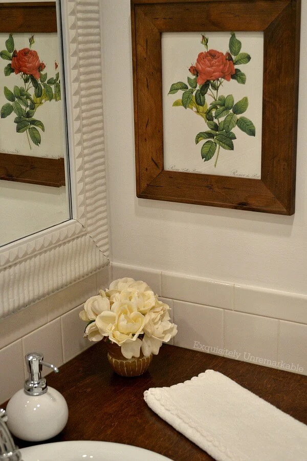 Red rose print framed on wall in bathroom with flower pot on wooden vanity top