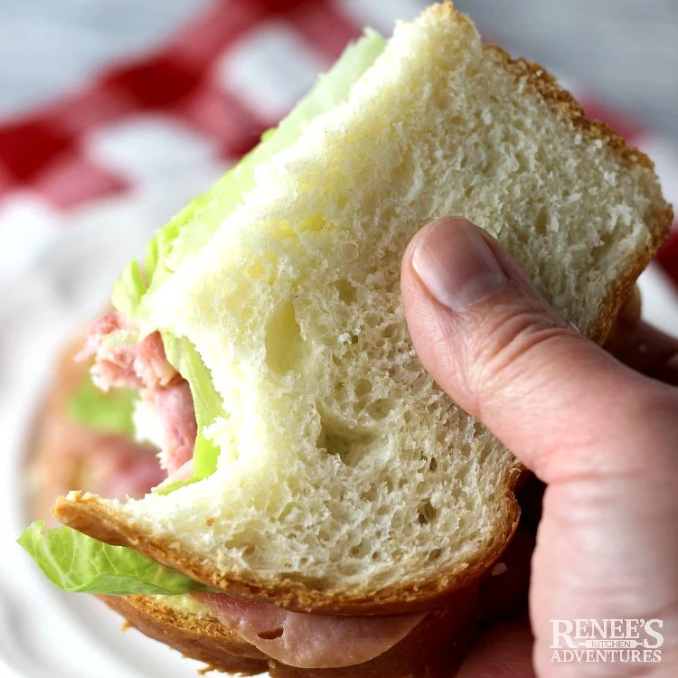 Half of a sandwich being held with a bite made from soft white bread