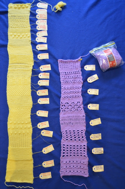 Two sampler strips of tricot stitches, arranged vertically on a royal blue polar fleece blanket. The yellow strip on the left has 20 different textured tricot stitch patterns. The lavender strip on the right has eight different lacy tricot stitch patterns. The strips have paper tags attached on their right-hand edges to signify the names of each stitch pattern. The tags are joined by thin threads of yellow sewing thread.