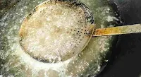 Pressing bhature under hot oil with a skimmer