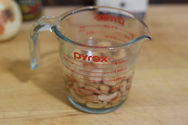A measuring cup full of cashews soaking in water.