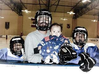 Father standing next to his 2 sons in hockey gear with 1 baby son in his arms
