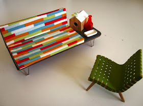 Mid century modern miniature sofa with attached coffee table and Jens Risom armchair, On the coffee table are mid century accessories including a bird house, bird, bottle and dish.