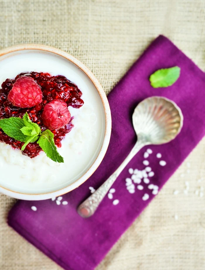An overview close up of Creamy Rice Pudding with Raspberry Compote in a bowl next to a purple napkin and spoon