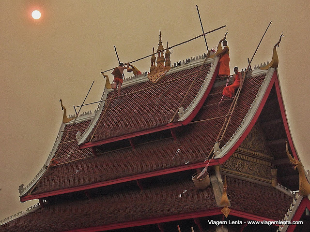 Sem proteções, monges reparam o telhado de um templo em Luang Prabang