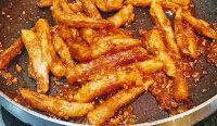 Stir frying potato fingers with honey chilli sauce for honey chilli potato recipe