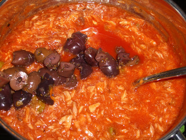 Foto van een pan met spaghettisaus puttanesca met zwarte olijven er bovenop