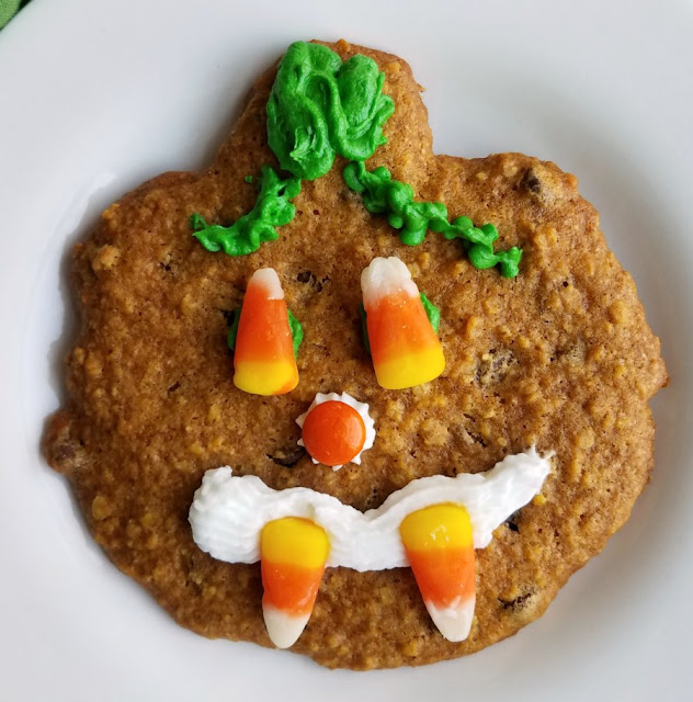 These fun pumpkin, oatmeal and chocolate chip cookies are a Halloween tradition in my family. We shape them like pumpkins and decorate them like jack-o-lanterns with candy faces! pumpkin shaped cookie with candy and frosting decoration to look like a jack-o-lantern