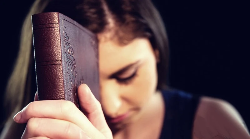 uma mulher segura uma bíblia e orar a Deus pedindo auxílio