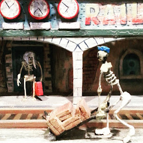 Model skeleton pushing a trolley of baggage at a miniature ghost train.