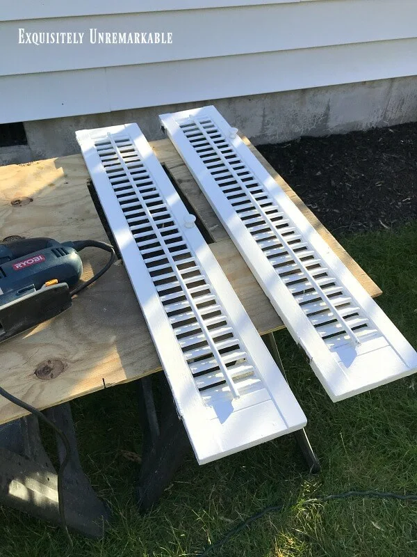 Two white shutters on a wooden board next to a saw