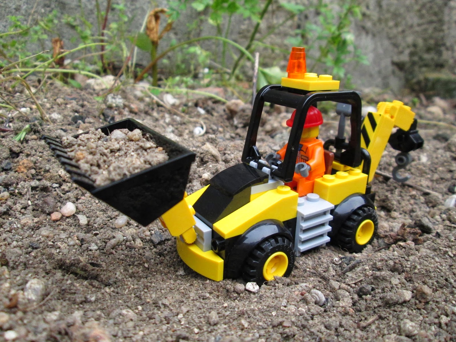 Diorama LEGO em cenário real, representando trabalhos de remoção de terras com máquina para substituição de rutura em conduta de água.