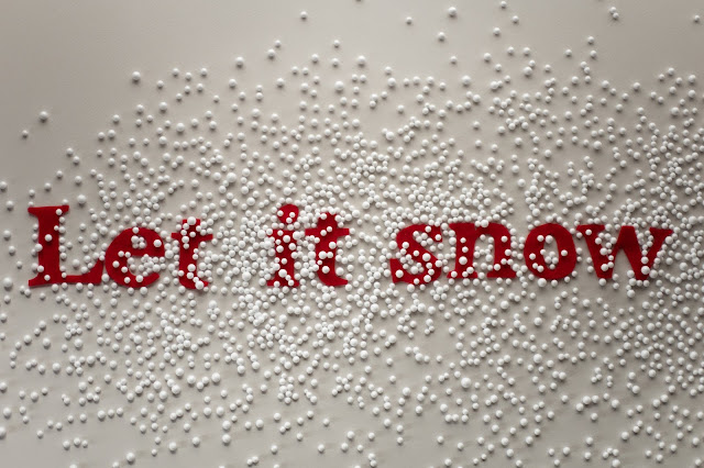 Letras en rojo formando la frase Let it snow con bolitas de porexpan simulando nieve por encima