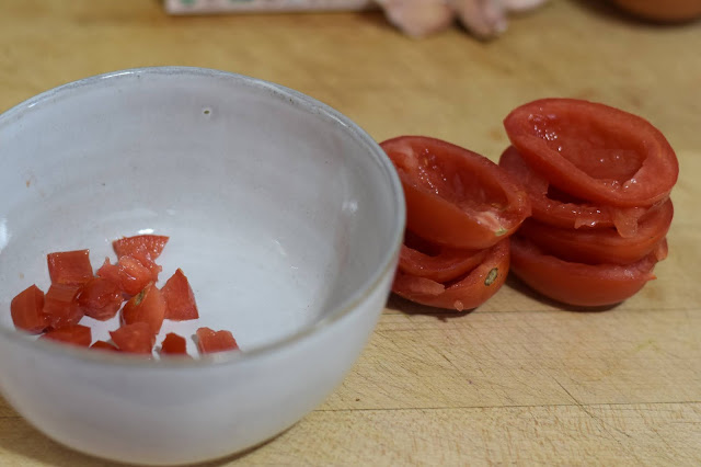Roma tomatoes being diced and put into a bowl.