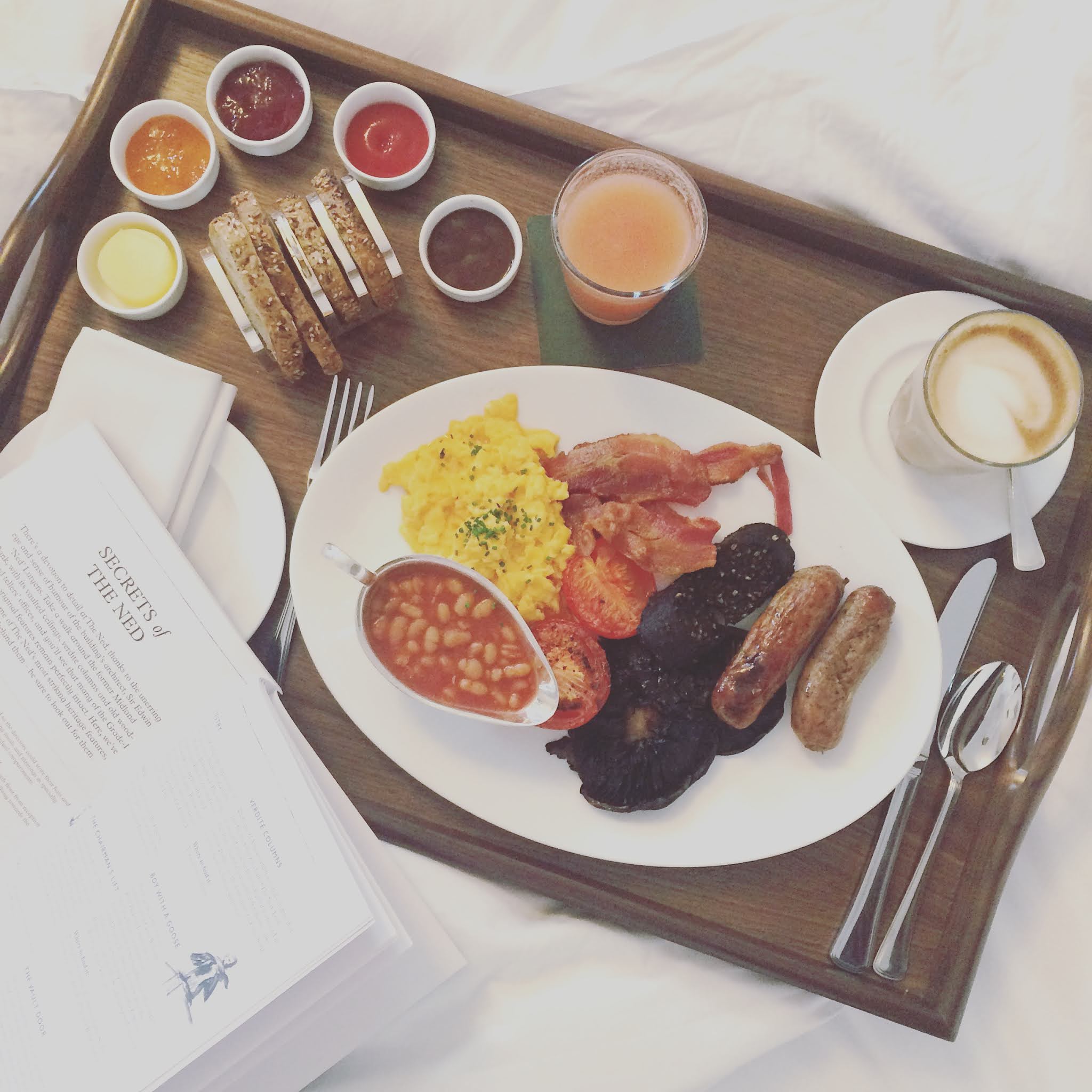 breakfast tray and coffee on a bed at the ned hotel London