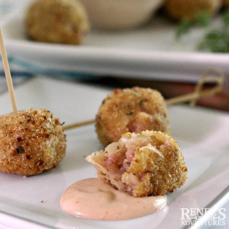 close up of a bite taken out of a sauerkraut ball showing inside sitting on a smear of dipping sauce and more sauerkraut balls in the back