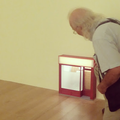 Large and empty room with a miniature lit storefront embedded into one corner of it.