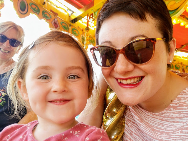 Picture of a 3 year old girl, her mummy and her grandma sat on horses on a carousel ride.