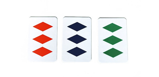 na zdjęciu trzy karty, tytułowy set, każda z kart ma po trzy symbole w innym kolorze, wszystkie mają kształt romba