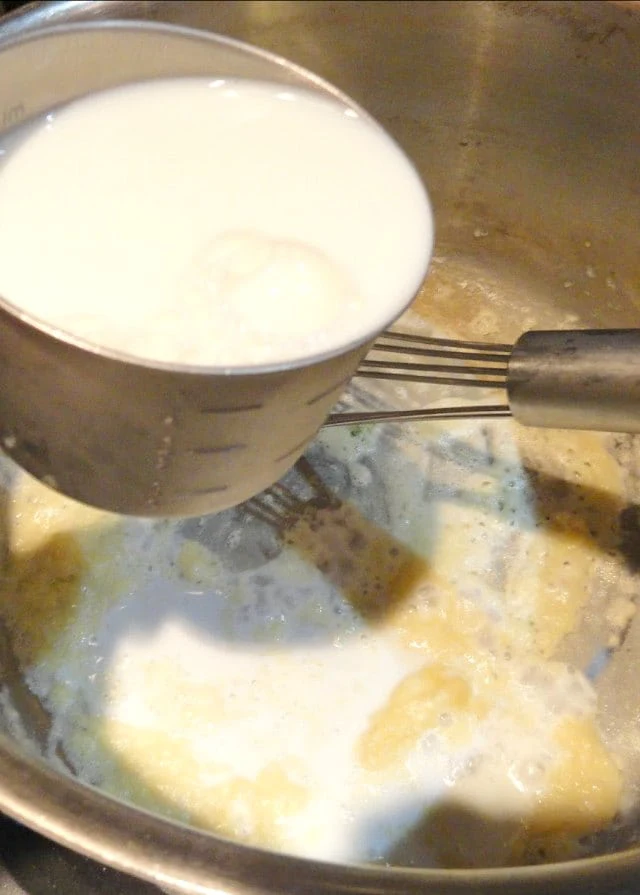 Milk being drizzled into flour roux mixture.
