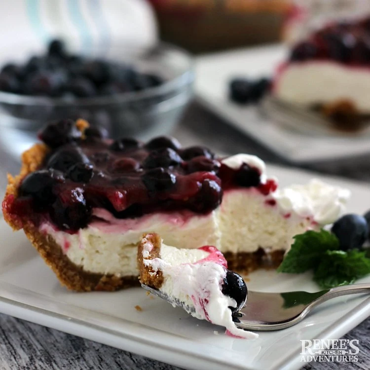 Slice of Blueberry Cream Cheese Pie by Renee's Kitchen Adventures on a white plate with a fork and fresh blueberries in the background