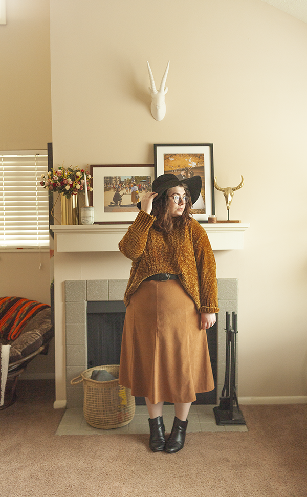 An outfit consisting of black floppy hat, dark yellow chenille sweater tucked into a brown a-line maxi skirt and black Chelsea boots.