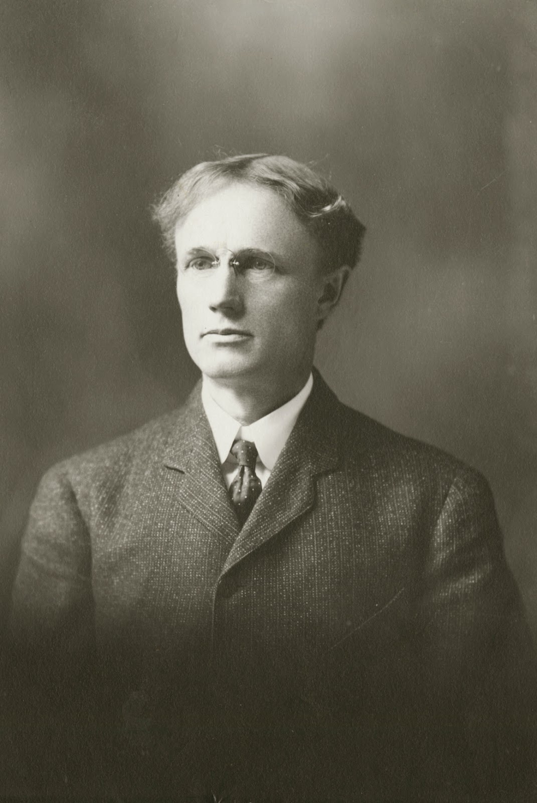 A black and white photograph of a white man with glasses.