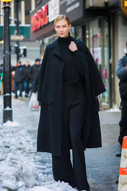 A woman wear a long black coat, based with a black shirt.