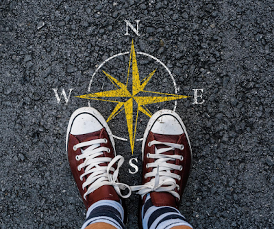 a pair of red converse stand on top of a compass drawn on an asphalt road