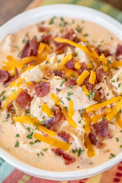 Slow Cooker Low-Carb Crack Chicken Soup - chicken soup loaded with cheddar, bacon, and ranch. Super easy to make - just dump everything in the slow cooker and let it do all the work. Chicken, cream cheese, chicken broth, bacon, ranch dressing mix, cheddar cheese. Can add spinach or broccoli to soup mixture. Delicious even if you aren't doing a keto/low-carb diet. #soup #slowcooker #crockpot #chicken #lowcarb #keto bowl of chicken soup topped with cheese and bacon