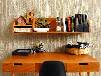 Modern dolls' house scene of a mid-century modern desk with shelf above holding a selection of books and magazines plus various industrial-style ornaments in browns and blacks,