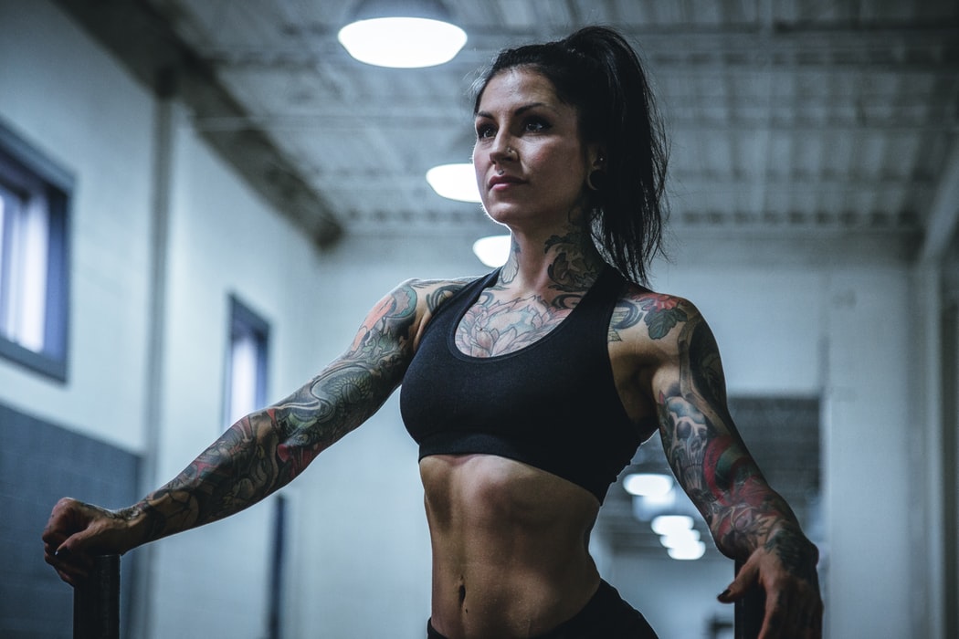 Imagen de chica tatuada musculosa posando con discos de peso