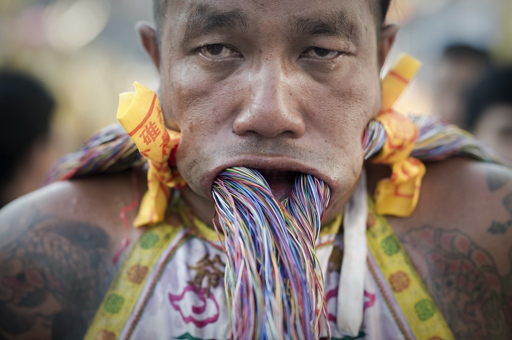 70 Of The Most Touching Photos Taken In 2015 - A devotee of the Chinese Bang Neow shrine pierces his cheeks with electrical wire to celebrate the annual vegetarian festival in Phuket, Thailand. The painful acts are said to purify participants.