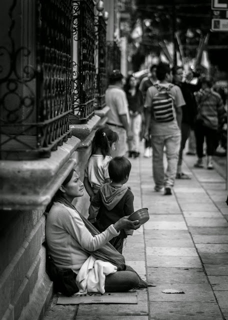 Una pobre mujer y su pequeño hijo pidiendo una moneda en una sociedad que no los mira.