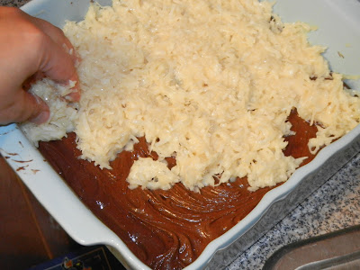 adding coconut mixture to top of brownies in a white baking dish 
