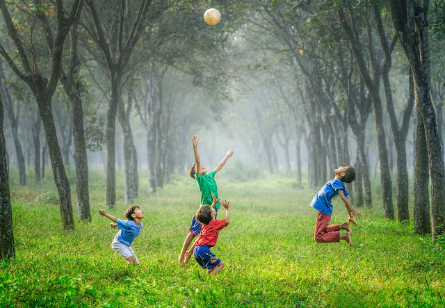 Children jumping to catch a ball in a forest