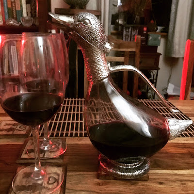 A decanter shaped like a duck, plus a glass of red wine.