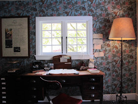 Inside view of an arts-and-crafts-style cottage, with a desk and chair under a window.
