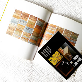 Art book open on a white bedspread with a flyer containing pictures of four works of art inserted between the two pages on display.
